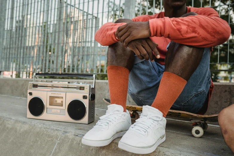 a man sitting on top of a skateboard next to a boombox, wearing white sneakers, orange tones, wearing white clothes, official product photo