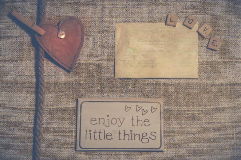 there is a sign that says enjoy the little things, by Emma Andijewska, trending on pixabay, mail art, cosy atmosphere, stop motion, brown, promo image