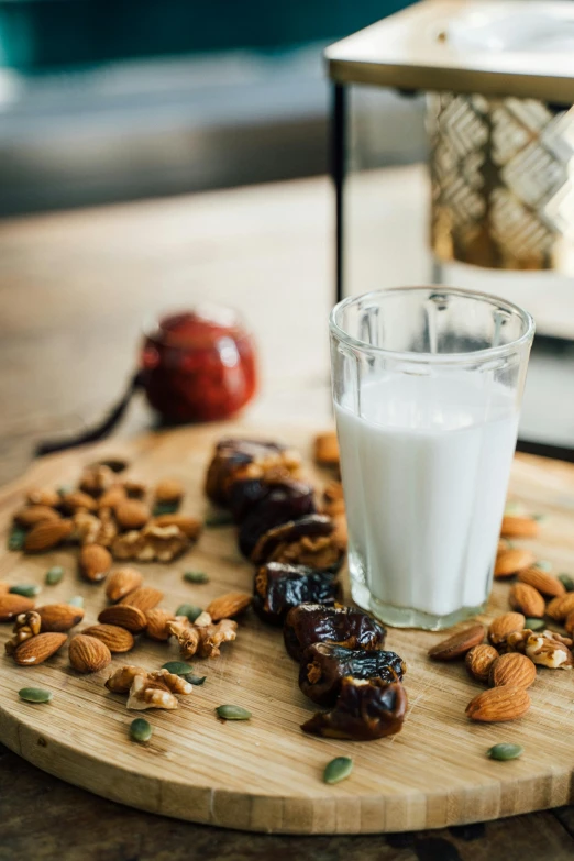 a glass of milk sitting on top of a wooden cutting board, by Julia Pishtar, hurufiyya, date, middle eastern details, ingredients on the table, nut