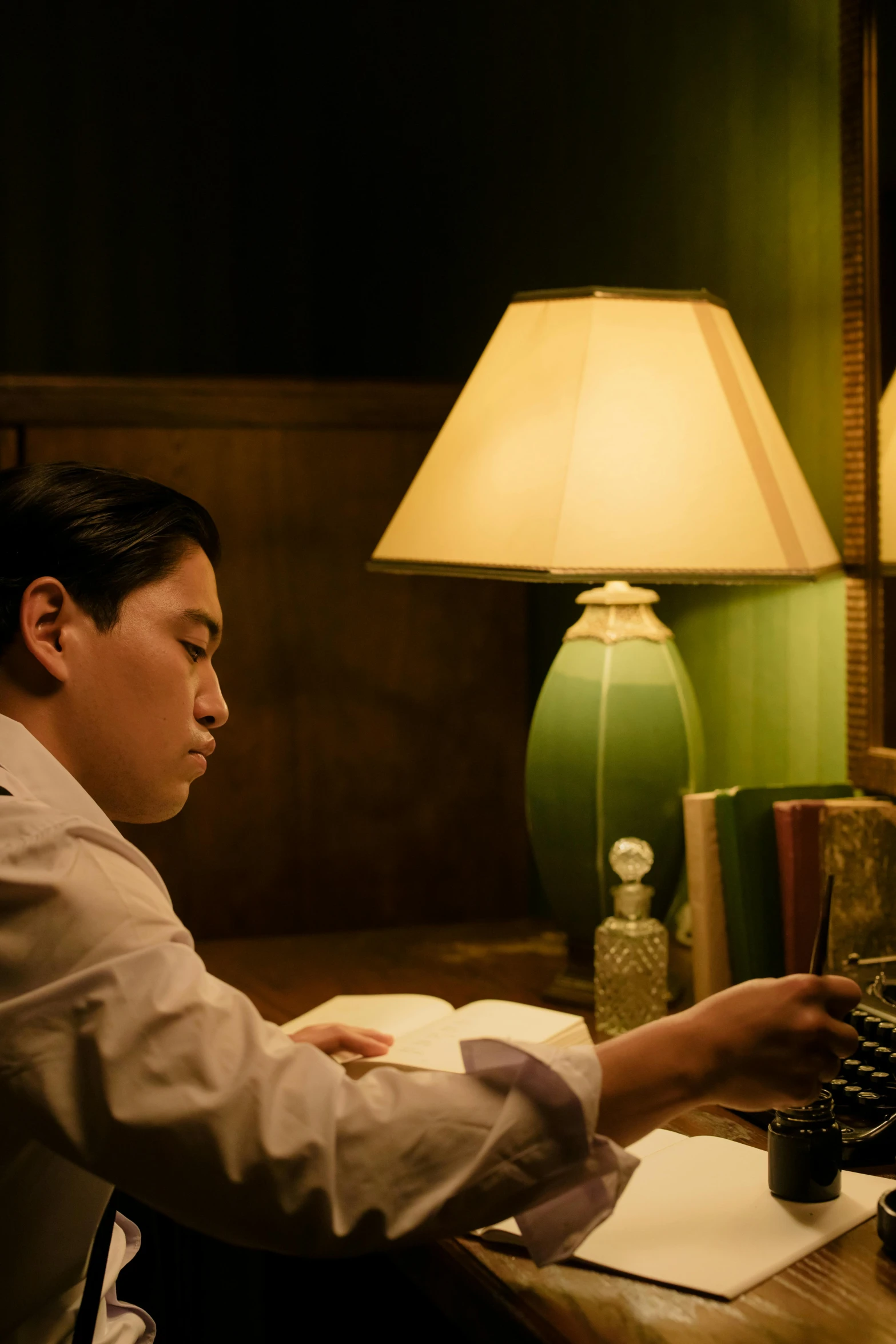 a man sitting at a desk in front of a computer, inspired by Li Tiefu, fantastic realism, film noir lighting, still from a wes anderson movie, asian male, writing a letter