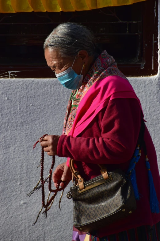 a woman wearing a face mask walking down a street, by Peter Churcher, pexels contest winner, cloisonnism, doing a prayer, ropes and chains, profile image, in a village street