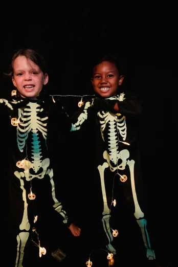 a couple of kids standing next to each other, by Ellen Gallagher, process art, glowing bones, diverse costumes, slide show, recital