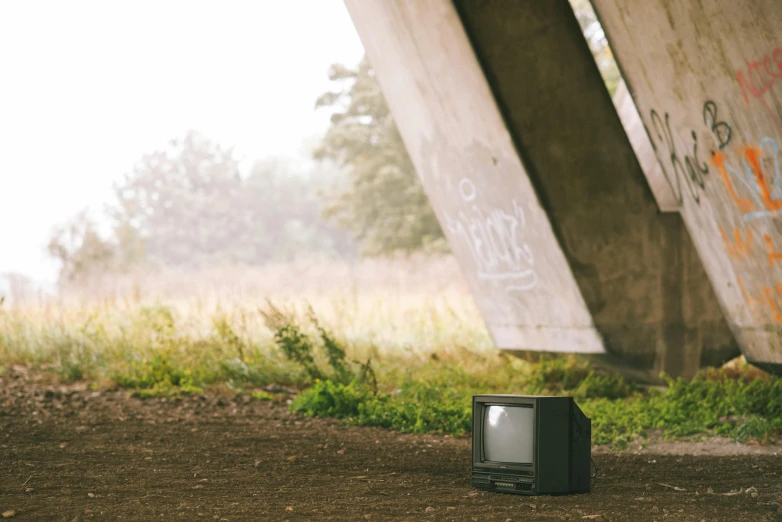 a small television sitting on top of a dirt field, a cartoon, unsplash, sitting under bridge, 1 9 8 0 s photo, vandalism, a green