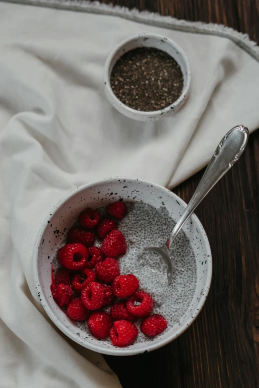 a bowl of raspberries next to a bowl of chia seeds, a still life, inspired by Jan Müller, trending on pexels, made of glazed, breakfast, grey and silver, petite