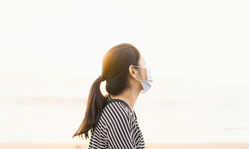 a woman wearing a face mask on the beach, trending on pexels, soft light from the side, zezhou chen, plain background, avatar image