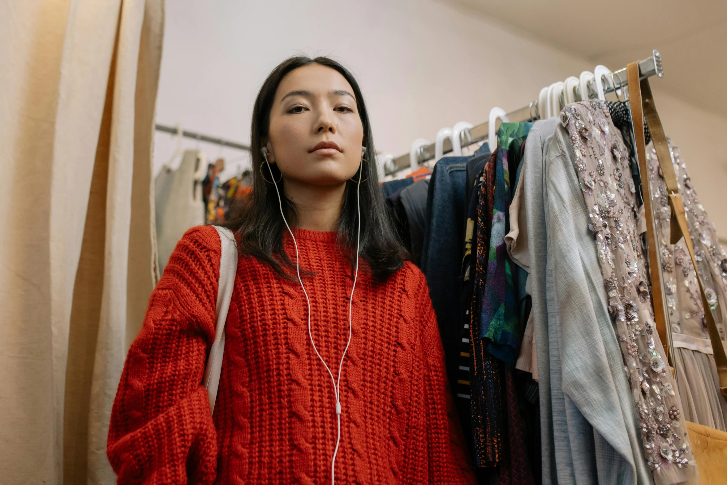 a woman standing in front of a rack of clothes, trending on pexels, earbuds, wearing a red turtleneck sweater, asian descent, worn out clothes