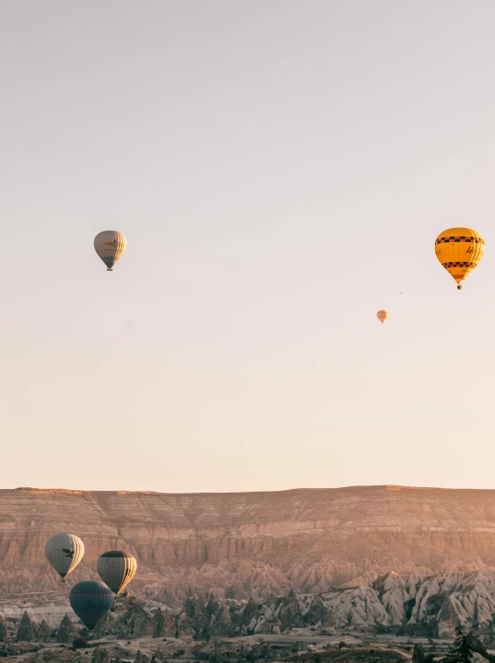 a group of hot air balloons flying over a valley, pexels contest winner, desert sunrise in the background, trending on vsco, shades of gold display naturally, spaceships in the sky