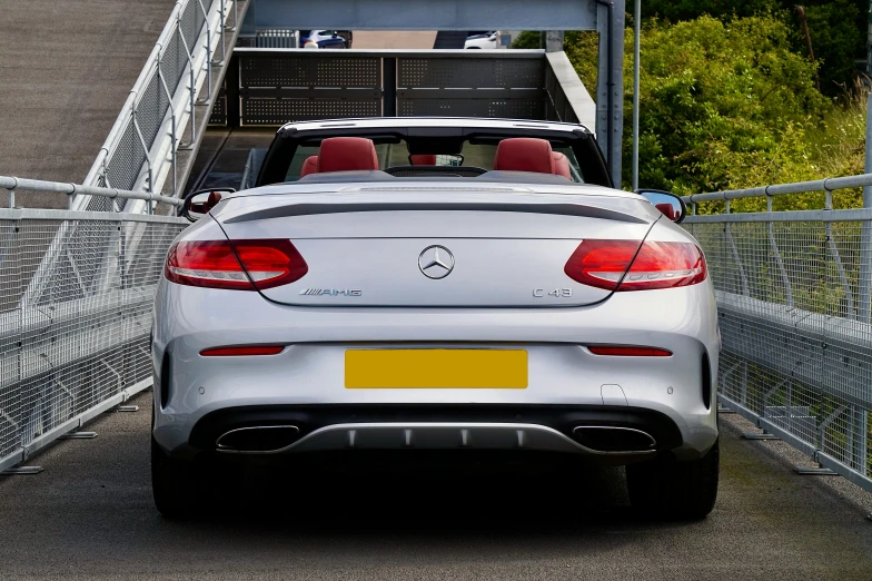 a silver car is parked on a bridge, convertable, rear facing, mercedez benz, glossy white metal