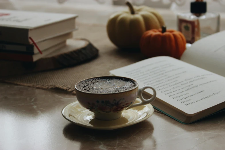 a cup of coffee and a book on a table, a still life, by Carey Morris, pexels contest winner, pumpkin, background image, thumbnail, angled shot