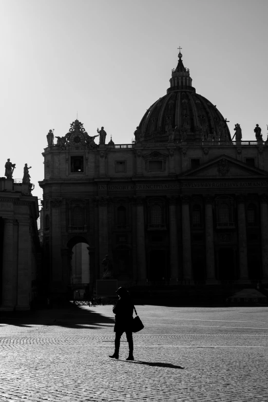 a black and white photo of a person standing in front of a building, by Cagnaccio di San Pietro, pexels contest winner, empire silhouette, catholic, people walking around, late afternoon