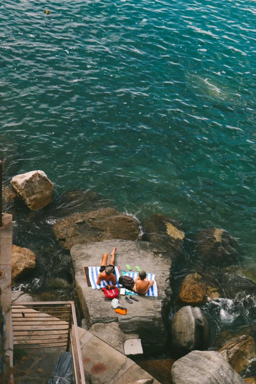 a couple of people laying on top of a rock next to a body of water, cinq terre, flatlay, picnic, small dock