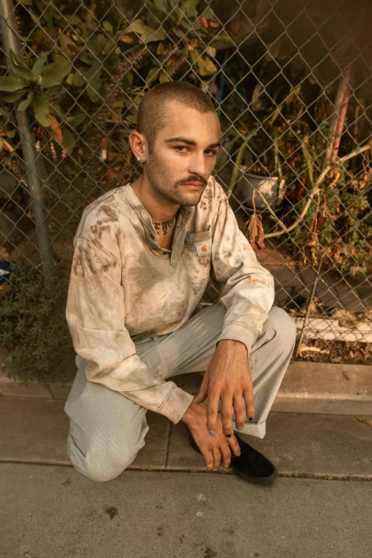 a man sitting on the ground next to a skateboard, an album cover, inspired by Elsa Bleda, photorealism, brown buzzcut, wearing prison jumpsuit, dirt stains, he got a big french musctache