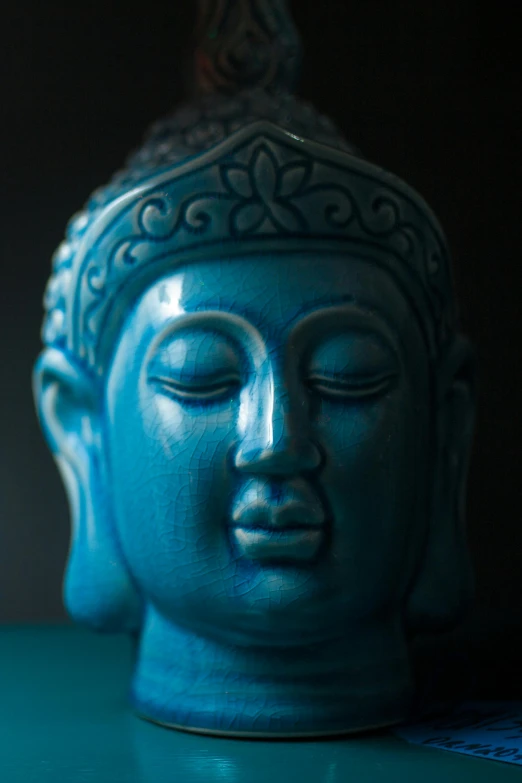 a blue buddha statue sitting on top of a table, closeup of the face, brilliantly coloured, face shown, shot on 70mm