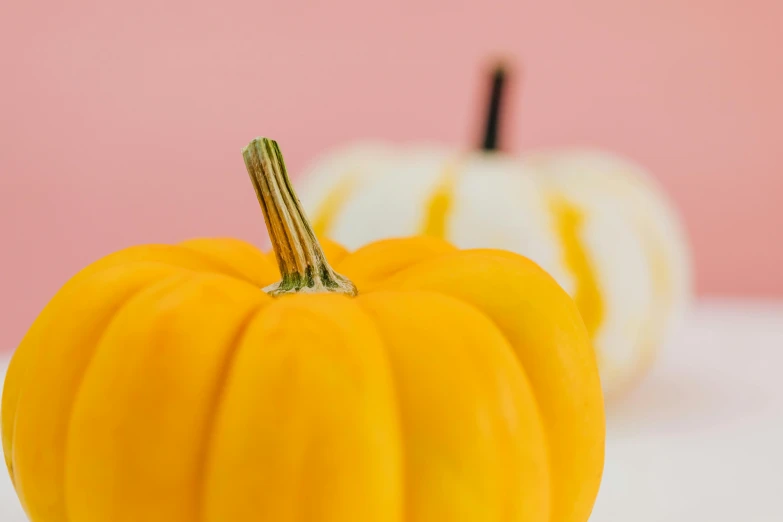 a couple of fake pumpkins sitting on top of a table, a macro photograph, inspired by Sarah Lucas, unsplash, yellow background, close-up product photo, white, pink and yellow