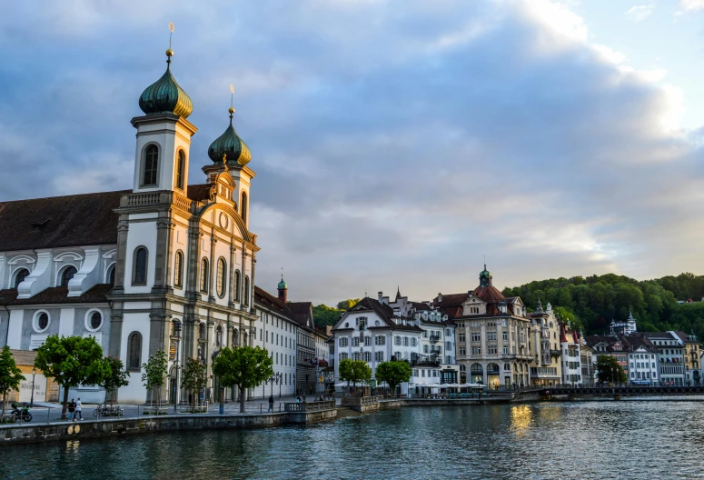 a large white building next to a body of water, by Julia Pishtar, pexels contest winner, renaissance, swiss architecture, early evening, black domes and spires, square