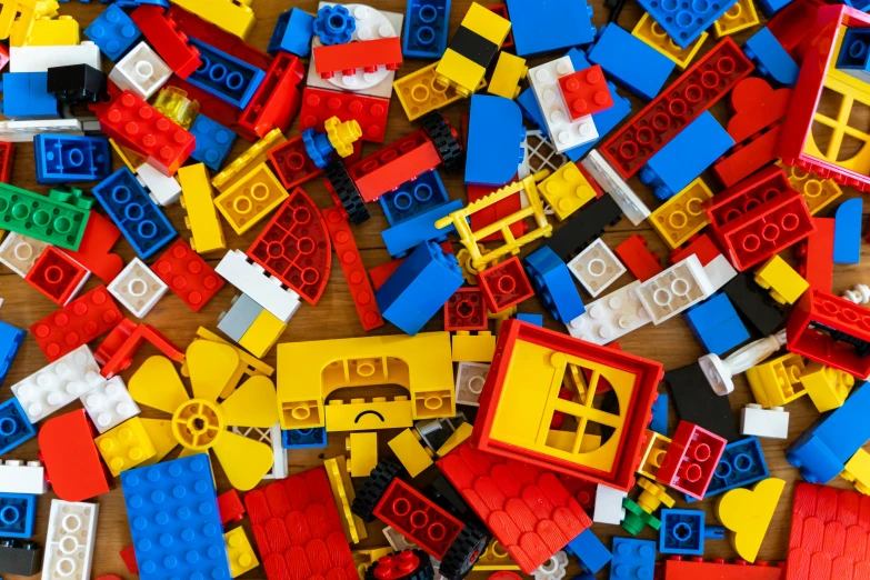 a pile of legos sitting on top of a wooden table, red yellow blue, miscellaneous objects, no logo, square