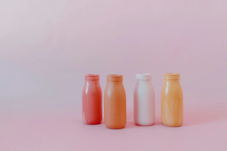 three bottles sitting next to each other on a pink surface, trending on unsplash, colored milk tea, light red and orange mood, in a row, bottles covered in wax