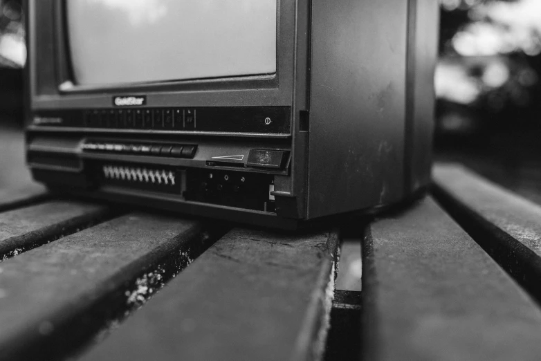 a television sitting on top of a wooden bench, a black and white photo, by Kristian Zahrtmann, unsplash, video art, close up shot a rugged, old computer, rack focus, black plastic