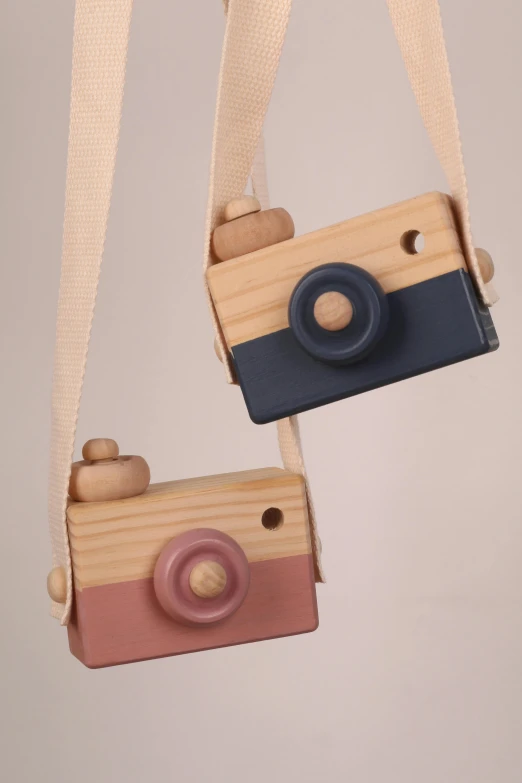 a couple of wooden cameras hanging from a string, 3 colours, two tone, navy, product shot