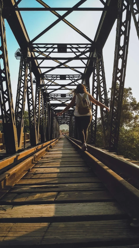 a person riding a bike across a bridge, an album cover, inspired by Steve McCurry, unsplash contest winner, teenage girl, railroad, australian, ((rust))