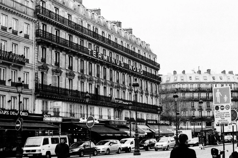 a black and white photo of a busy city street, a black and white photo, paris school, gorgeous buildings, 4x5 styled street photography, lots of shops, luxurious