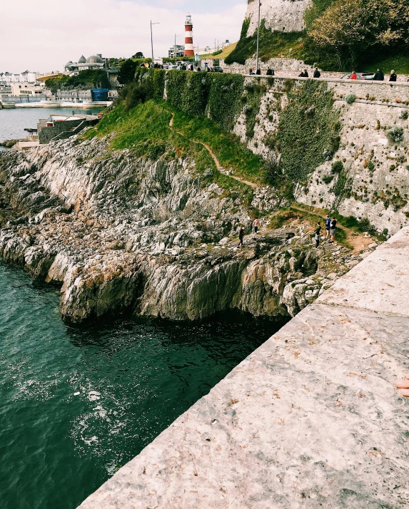 a man sitting on top of a rock next to a body of water, white marble buildings, instagram story, walking to the right, harbor