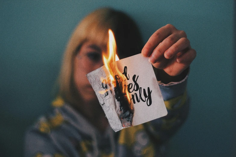 a woman holding a piece of paper with fire coming out of it, a polaroid photo, inspired by Elsa Bleda, trending on pexels, graffiti, chloe price, destroy lonely, a friendly wisp, lets get weird