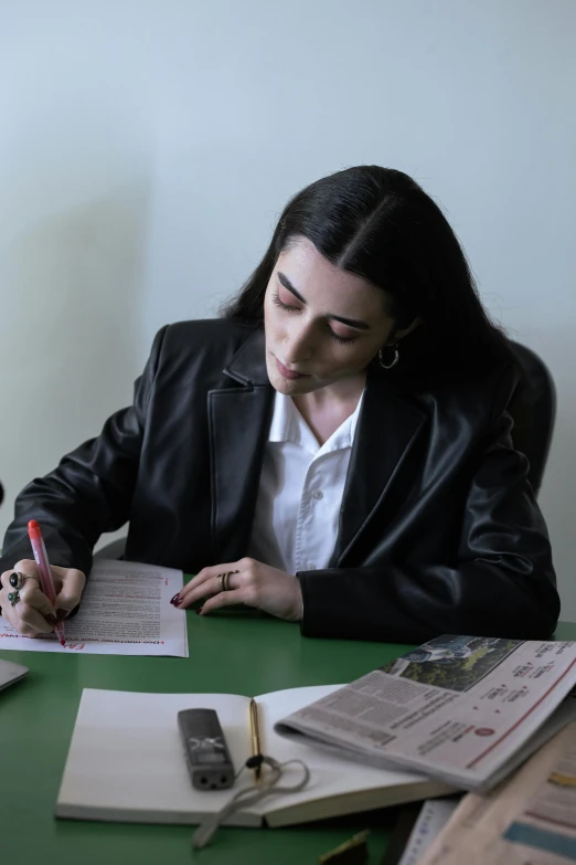 a woman sitting at a desk writing on a piece of paper, an album cover, inspired by Marina Abramović, pexels contest winner, academic art, a man wearing a black jacket, kurdish lawyer, lesbians, russian academic