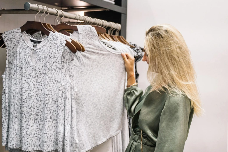 a woman standing in front of a rack of clothes, by Nicolette Macnamara, trending on pexels, happening, white and grey, wearing a designer top, federation clothing, people shopping