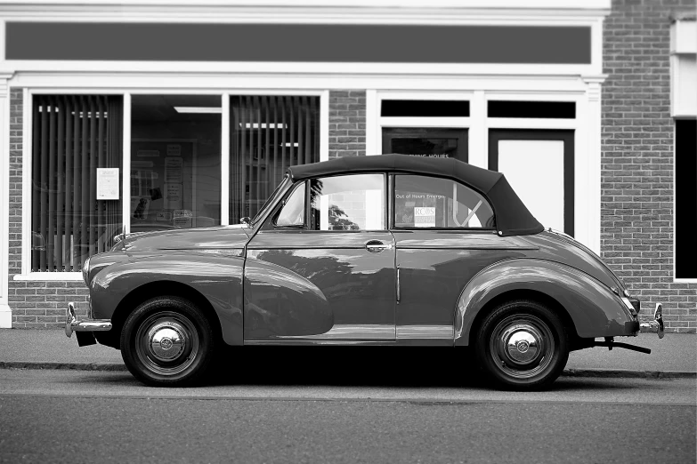 a black and white photo of a car parked in front of a building, by Dave Allsop, pexels contest winner, photorealism, soft top, square, retro colour, profile posing
