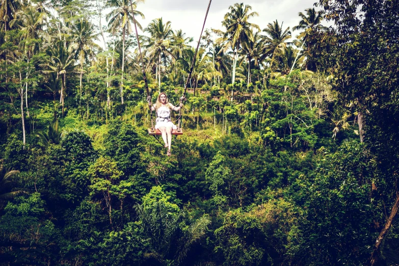 a woman riding a zipline over a lush green forest, sumatraism, lo - fi, conde nast traveler photo, 🦩🪐🐞👩🏻🦳, bali