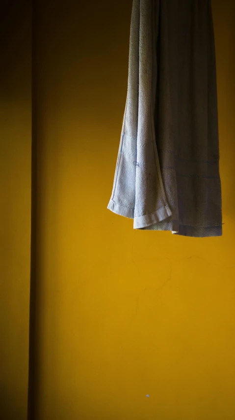 a white shirt hanging on a yellow wall, unsplash, grey tarnished robes, color ( sony a 7 r iv, curtain, indigo