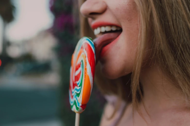 a close up of a person holding a lollipop, by Emma Andijewska, pexels contest winner, smiling :: attractive, unsplash 4k, giant mouth, edible crypto