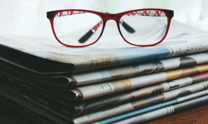 a stack of newspapers with glasses on top, a cartoon, by Carey Morris, pexels, square glasses, cinematic, high-quality photo, ultra definition