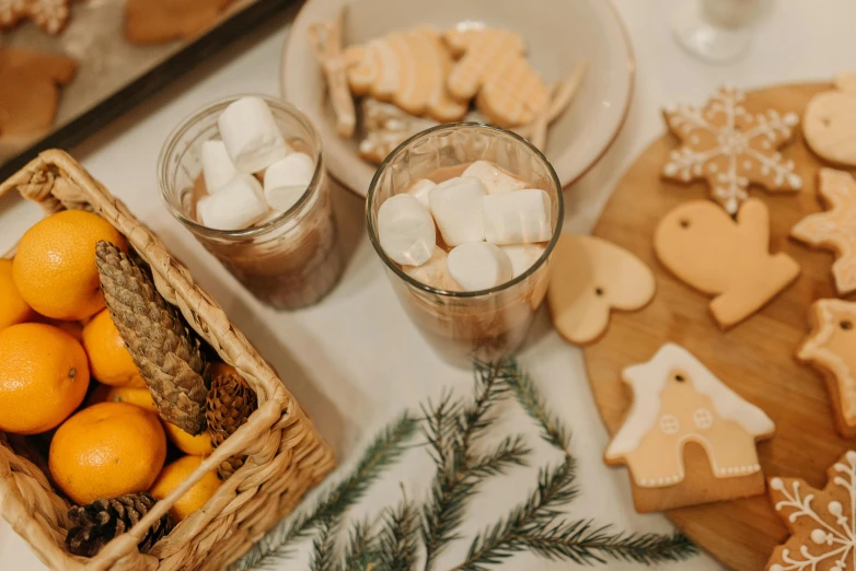 a table topped with a basket of oranges and cookies, by Emma Andijewska, pexels, folk art, hot cocoa drink, background image, marshmallows, abcdefghijklmnopqrstuvwxyz