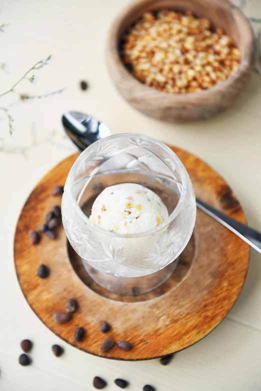 a cup of ice cream sitting on top of a wooden plate, seeds, with clear glass, displayed, lifestyle