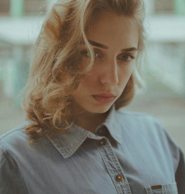 a woman in a denim shirt looking at her cell phone, an album cover, inspired by Elsa Bleda, pexels contest winner, pale skin curly blond hair, serious face, gif, handsome girl