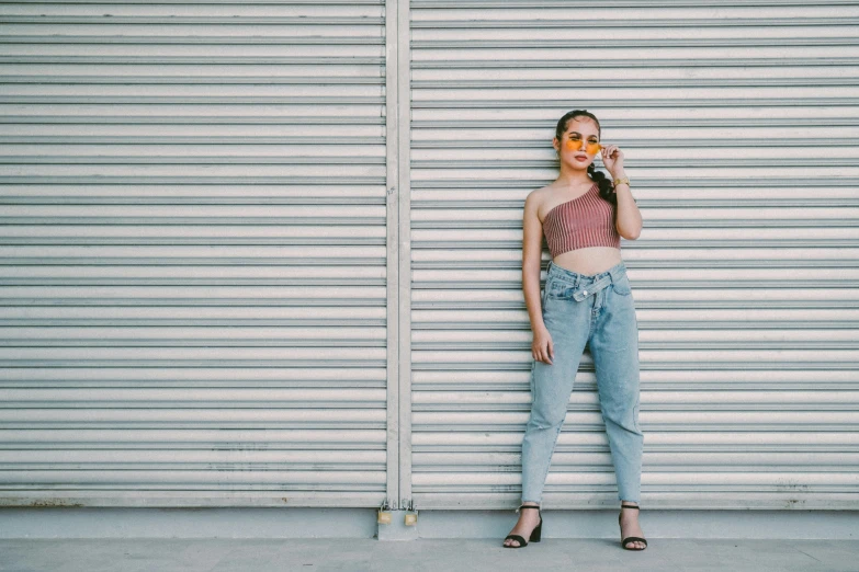 a woman standing in front of a garage door eating a donut, by Robbie Trevino, trending on pexels, baggy jeans, croptop, elegant girl in urban outfit, metallic shutter