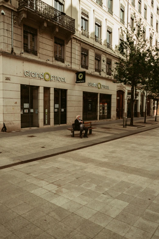 a man sitting on a bench in front of a building, by Cricorps Grégoire, trending on unsplash, clean streets, low quality photo, 1996), gigapixel photo