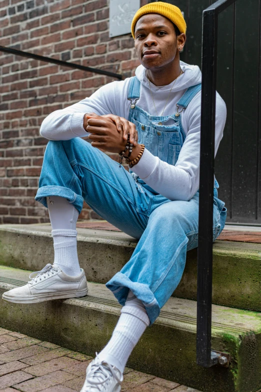 a man sitting on the steps of a building, wearing blue jean overalls, wearing off - white style, feet posing, in white turtleneck shirt