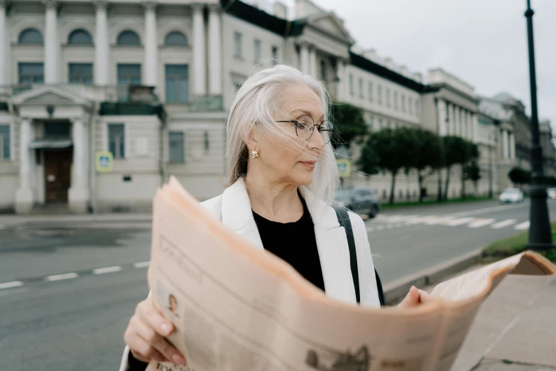 a woman reading a newspaper on a city street, a photo, by Emma Andijewska, pexels contest winner, white-haired, librarian, gif, valeriy vegera