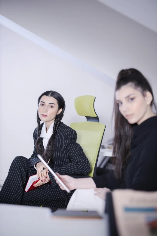 two women sitting next to each other in a room, an album cover, by Attila Meszlenyi, trending on pexels, in a business suit, dilraba dilmurat, sitting in office, portait image