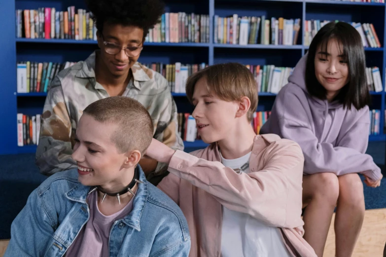 a group of young people sitting next to each other, a cartoon, trending on pexels, antipodeans, shaved head, in a library, queer woman, looking her shoulder