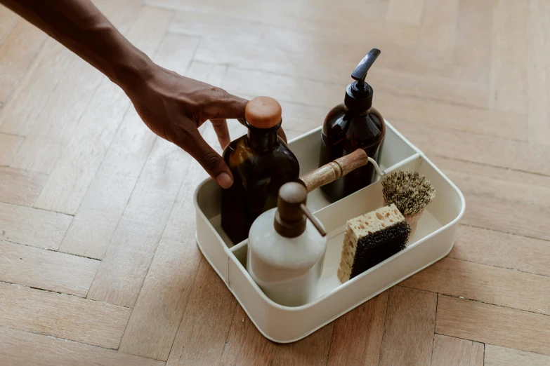 a person putting something in a container on the floor, a still life, inspired by Sarah Lucas, unsplash, photoshoot for skincare brand, carrying a tray, brown resin, bottle