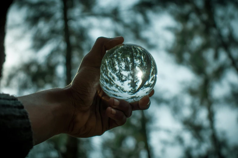 a person holding a crystal ball in their hand, by Jan Rustem, pexels contest winner, touching tree in a forest, marbles, silver light, glass shader