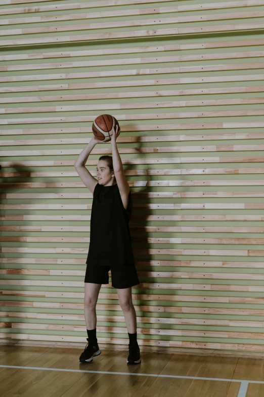 a young man holding a basketball on top of a wooden floor, she is wearing a black tank top, 155 cm tall, wearing black shorts, britt marling style 3/4