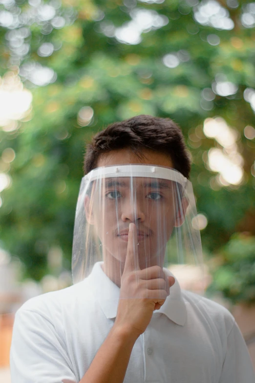 a man in a white shirt and a clear face shield, an album cover, pexels, south east asian with round face, technology cloak, hand over mouth, high school