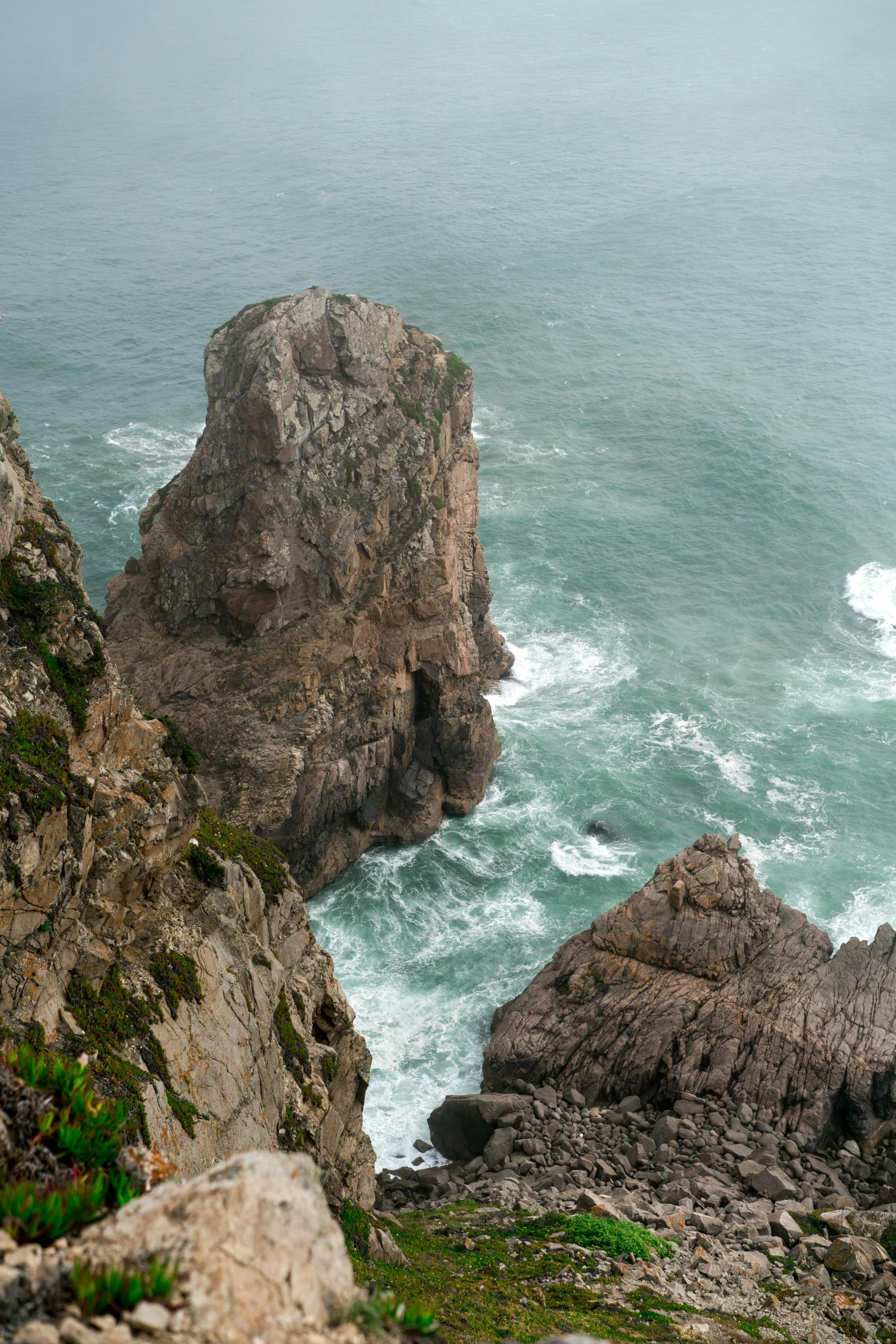 a man standing on top of a cliff next to the ocean, piroca, rock arcs, zoomed out to show entire image, tumultuous