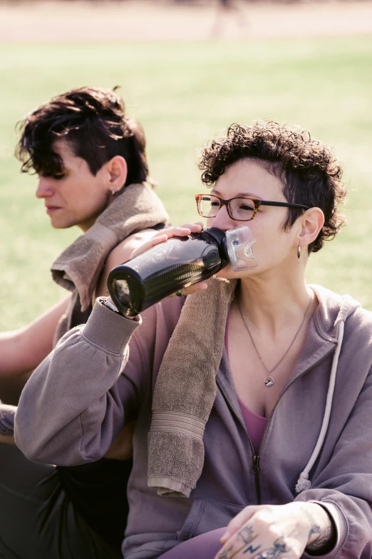 a woman drinking from a bottle while sitting next to a man, inspired by Nan Goldin, trending on pexels, renaissance, in a grassy field, lesbians, cold brew coffee ), curly haired