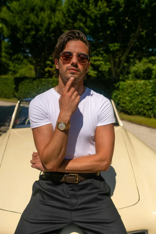 a man sitting on the hood of a car, a picture, inspired by Luca Zontini, holding gold watch, wearing shades, dressed in a white t shirt, promotional image